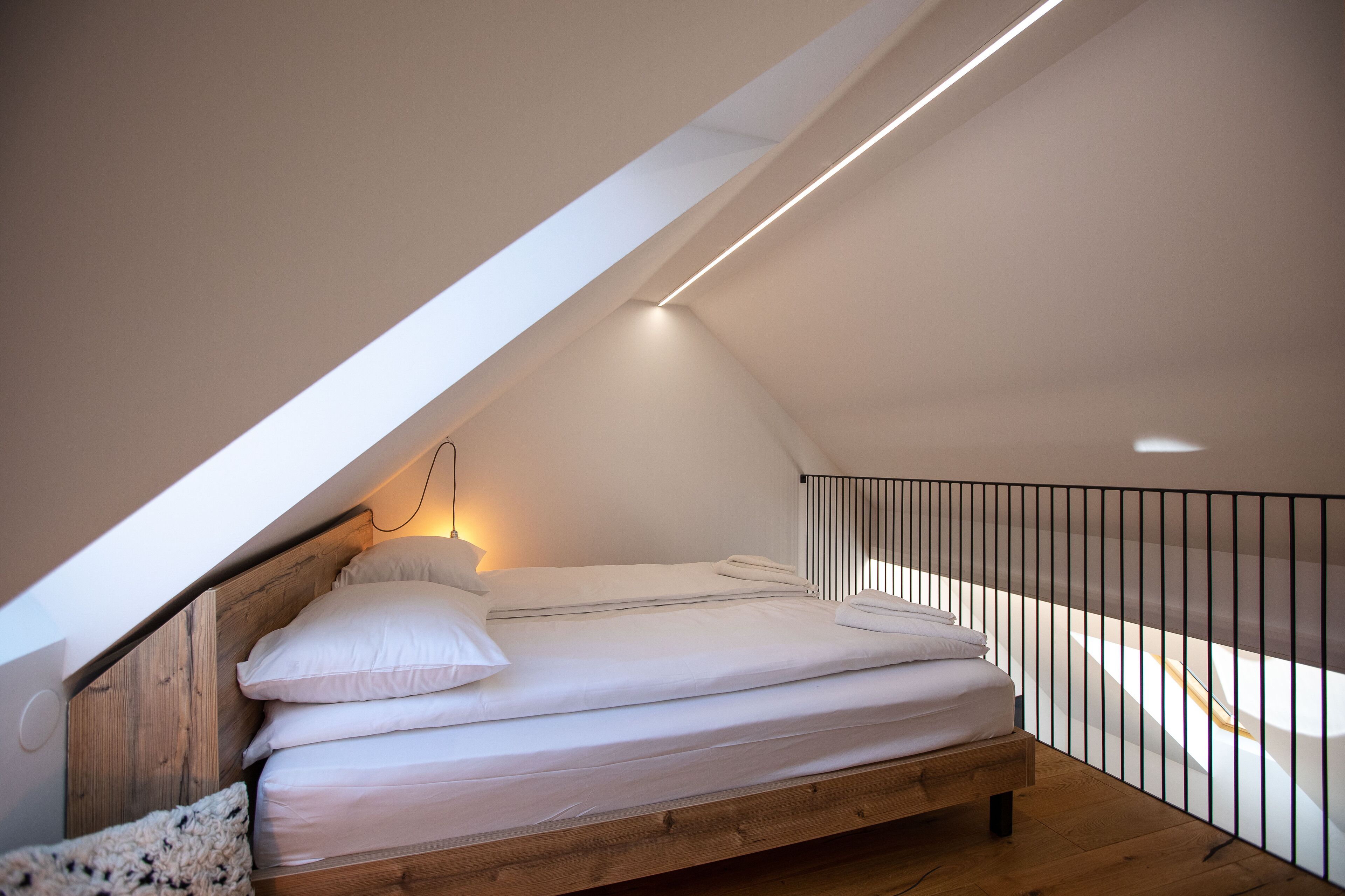 A loft bedroom with a sloped ceiling, a wooden bed frame, and a black railing.