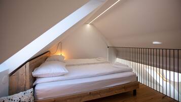 A loft bedroom with a sloped ceiling, a wooden bed frame, and a black railing.