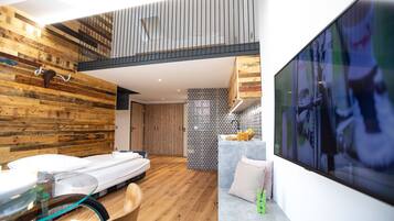 Un interior moderno con cama tipo loft, paredes de madera, zona de cocina y una amplia pantalla de televisión.