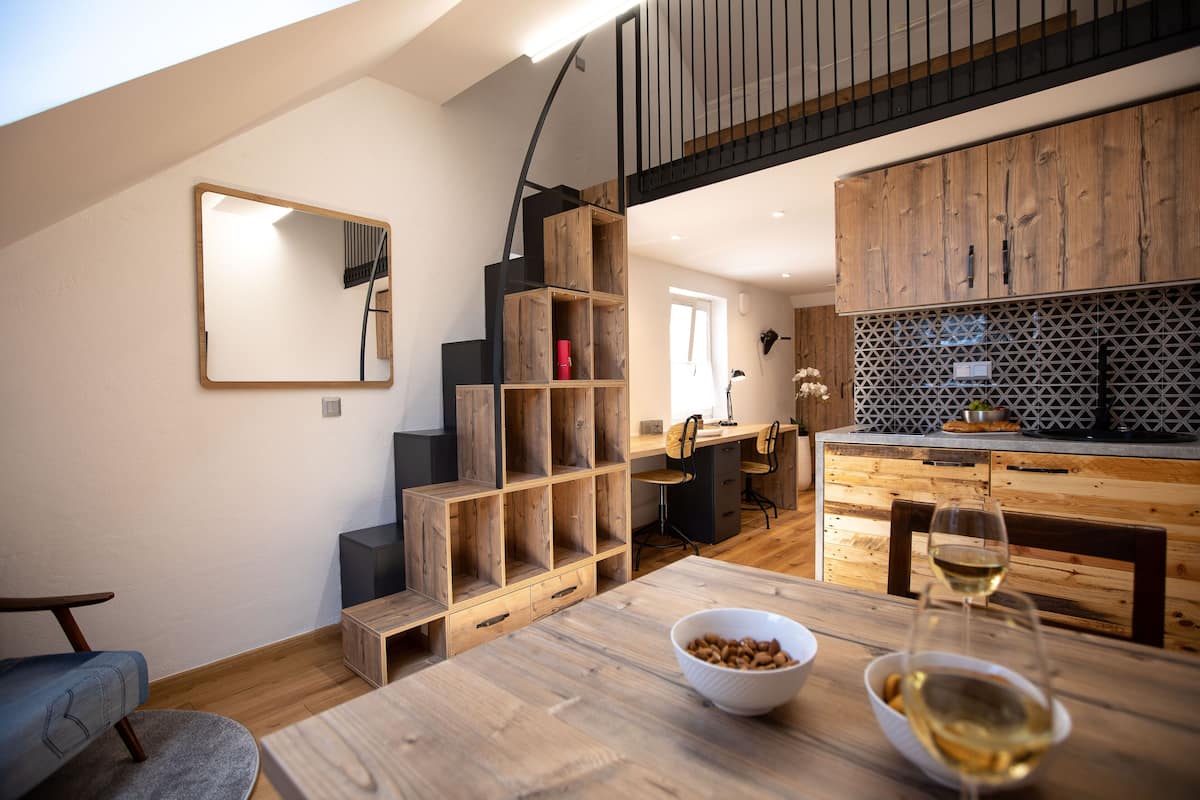 Une cuisine moderne avec des meubles en bois, un coin repas doté d’une table en bois et un escalier avec une rampe noire.