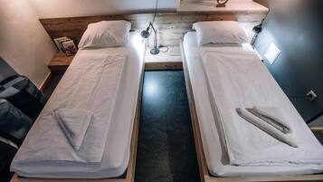 Habitación doble con dos camas individuales, cabecera de madera, una mesita de noche con lámpara y una ventana con cortinas.