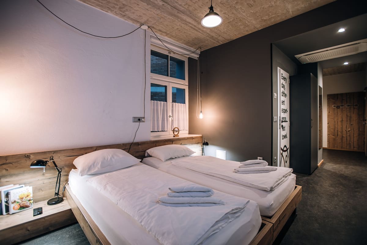 Une chambre d’hôtel avec deux lits, une fenêtre avec des rideaux, une lampe de chevet et une tête de lit en bois.