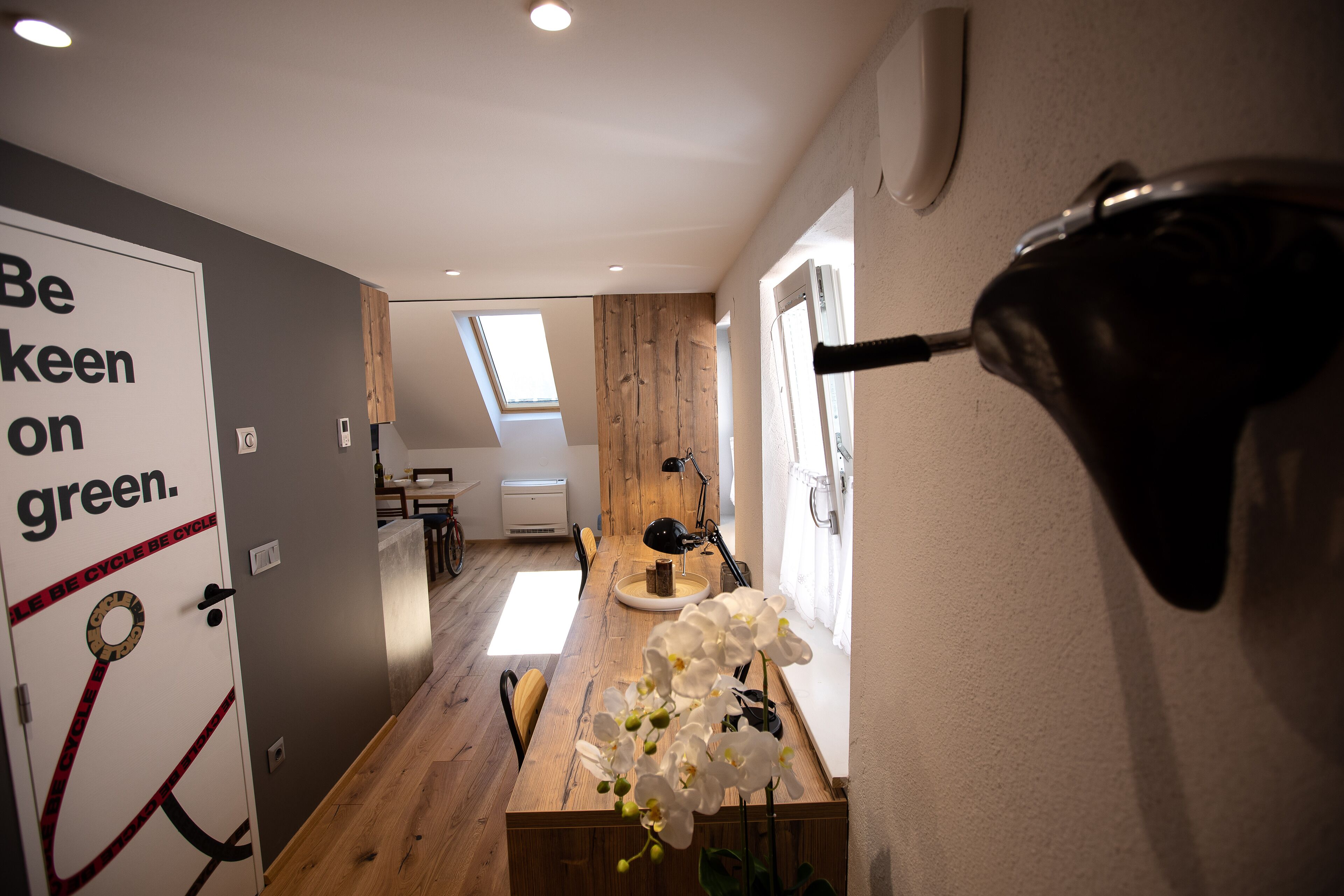 Ein modernes Interieur mit einem Holzesstisch, einer Wandleuchte und einer Tür mit einem Hinweisschild in Grüntönen.