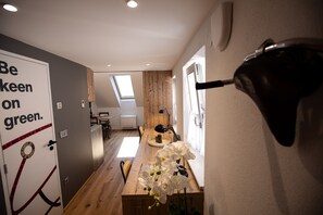 A modern interior with a wooden dining table, a wall-mounted lamp, and a door with a green-themed sign.