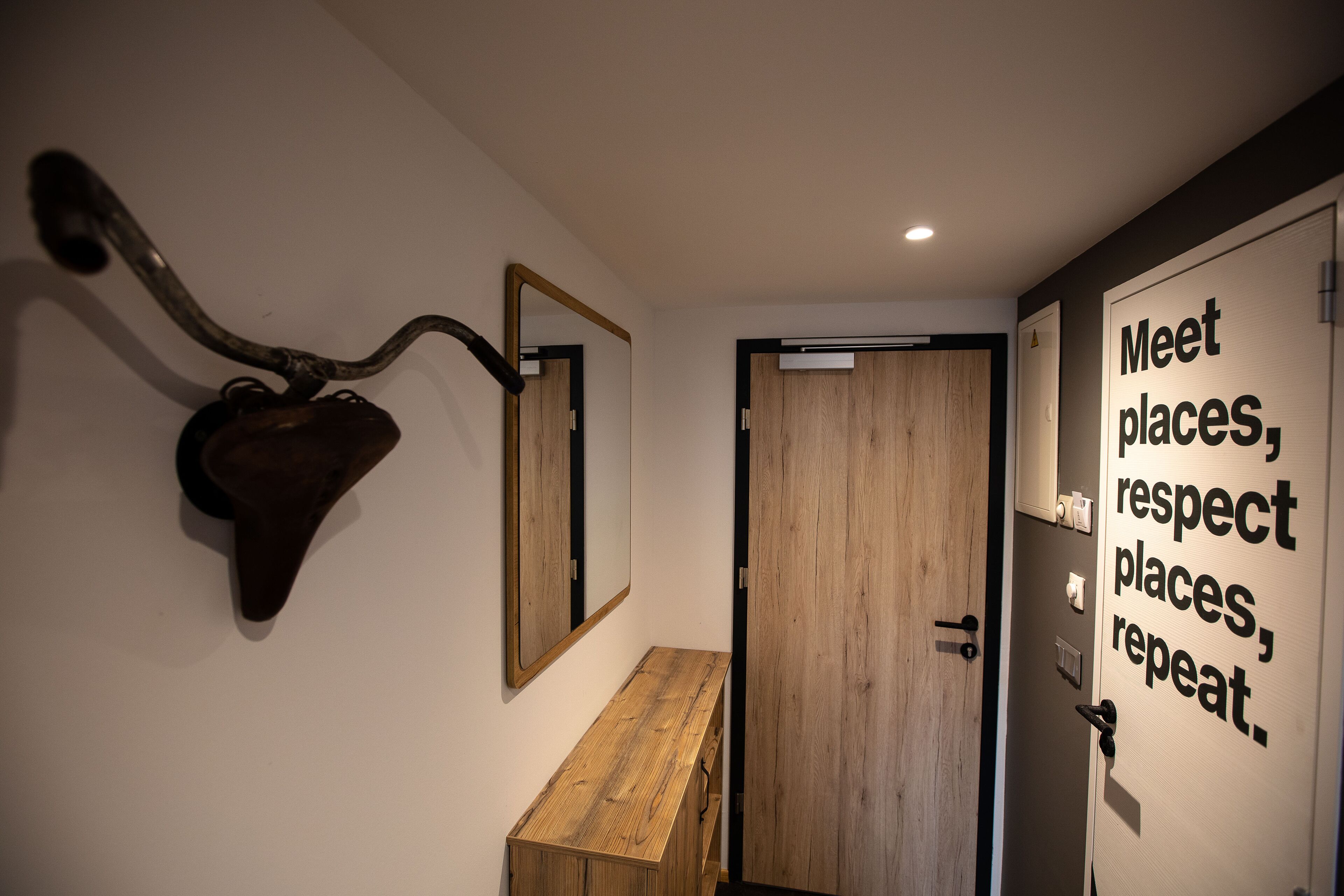 A hallway with a wooden bench, a wall-mounted mirror, and a door with a motivational quote.