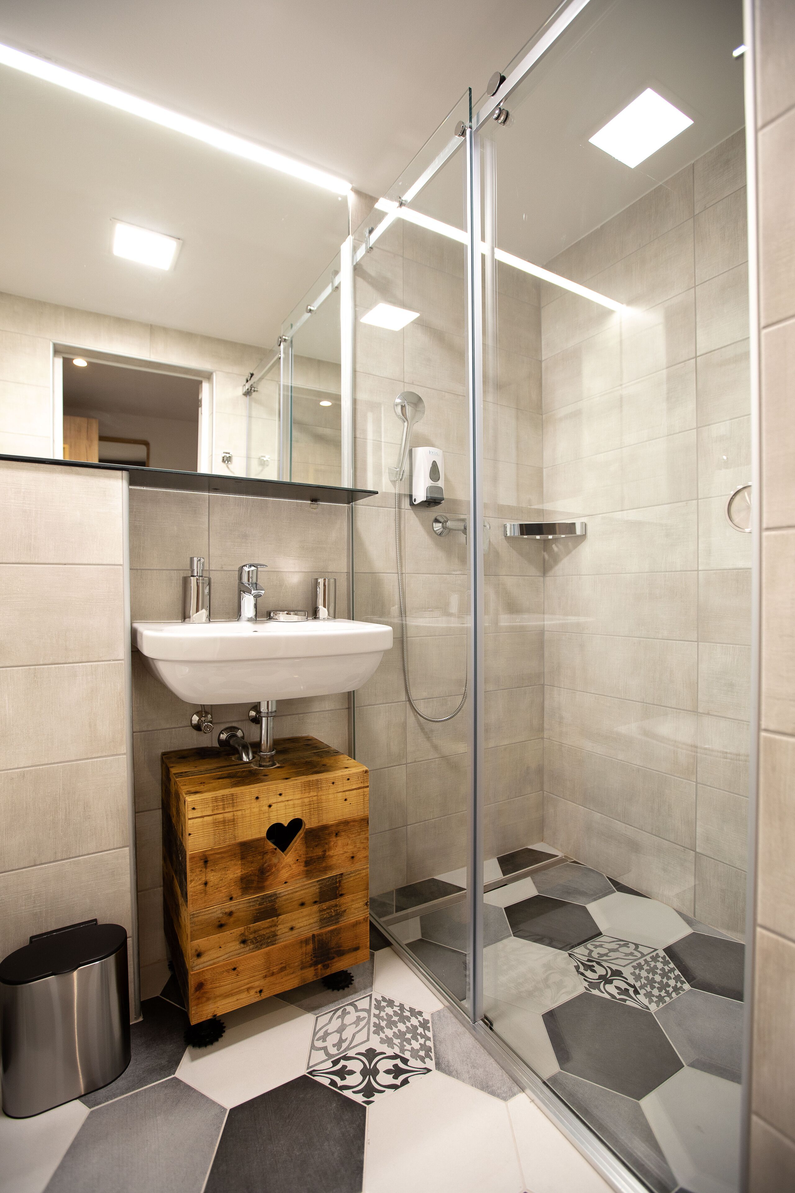 A modern bathroom with a glass-enclosed shower, a wooden chest of drawers, and a white sink.