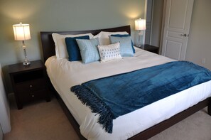 A neatly made bed with a blue throw blanket, white bedding, and multiple pillows. There are two bedside tables with lamps, a dark headboard, and a door in the background. - Luxury Modern Home With CDC Cleaning Standards, 2 Miles From Disney #6wh546 (Kissimmee)