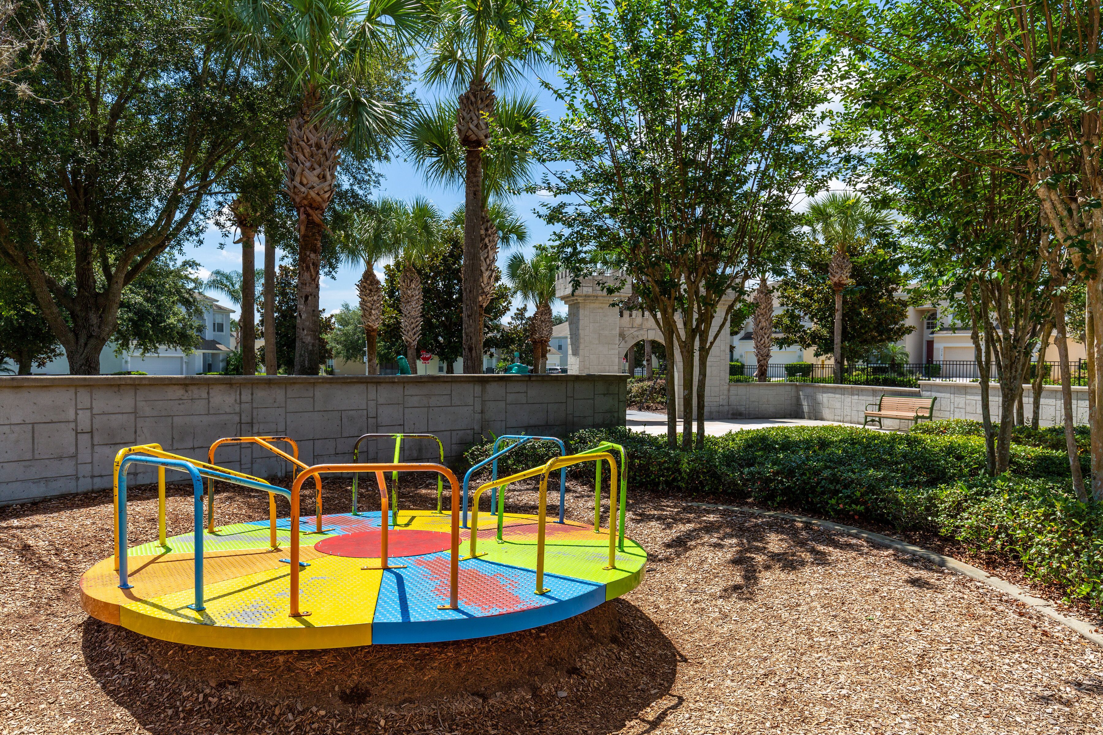 A playground with a colorful rotating platform and surrounding trees.