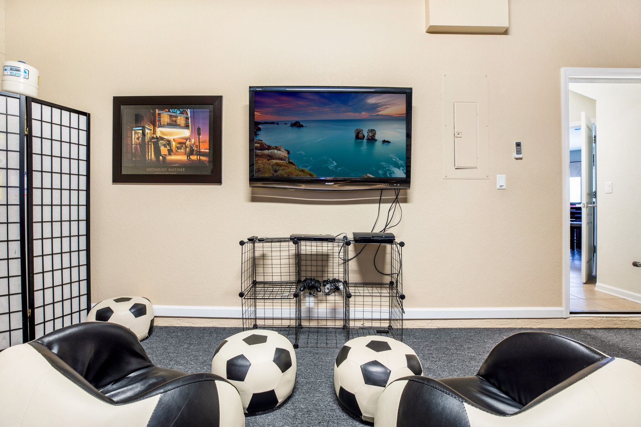 Une pièce équipée d’un téléviseur diffusant un paysage, d’une console de jeux et de deux canapés en cuir, avec des ballons de football à proximité.