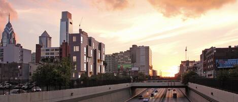 A multi-lane highway with vehicles, surrounded by modern buildings and a sunset sky.