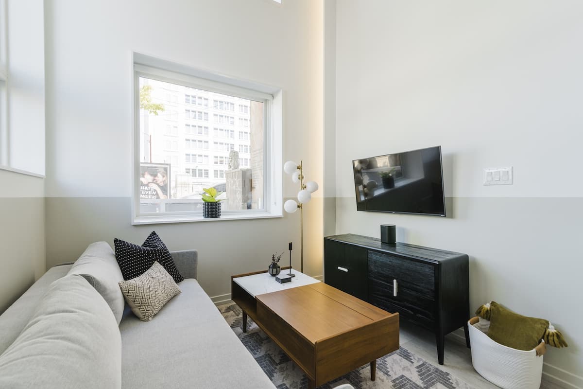 A modern living room with a sofa, coffee table, TV, and a window with a city view.