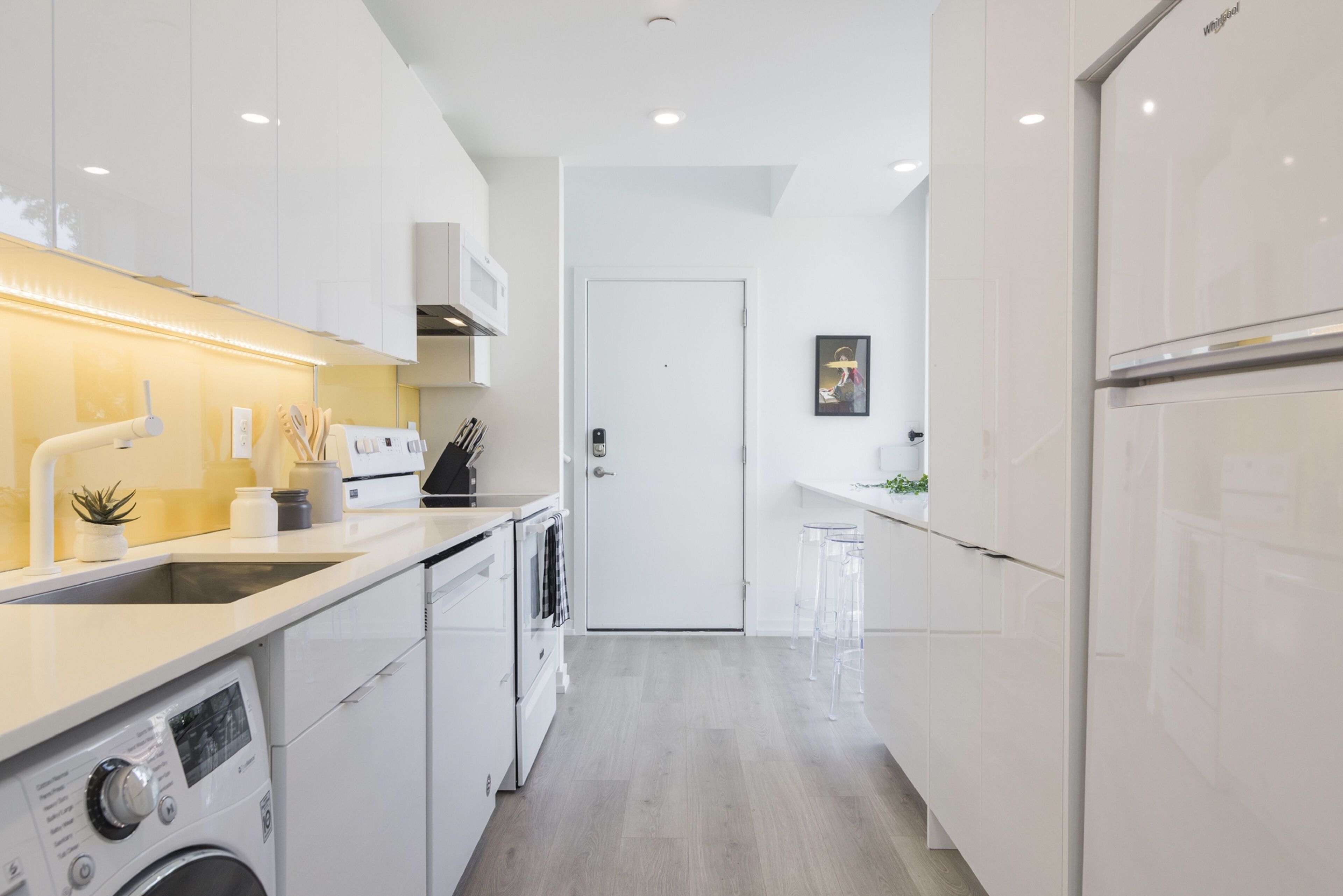 A modern kitchen with white cabinetry, a built-in oven, a washing machine, and a microwave.