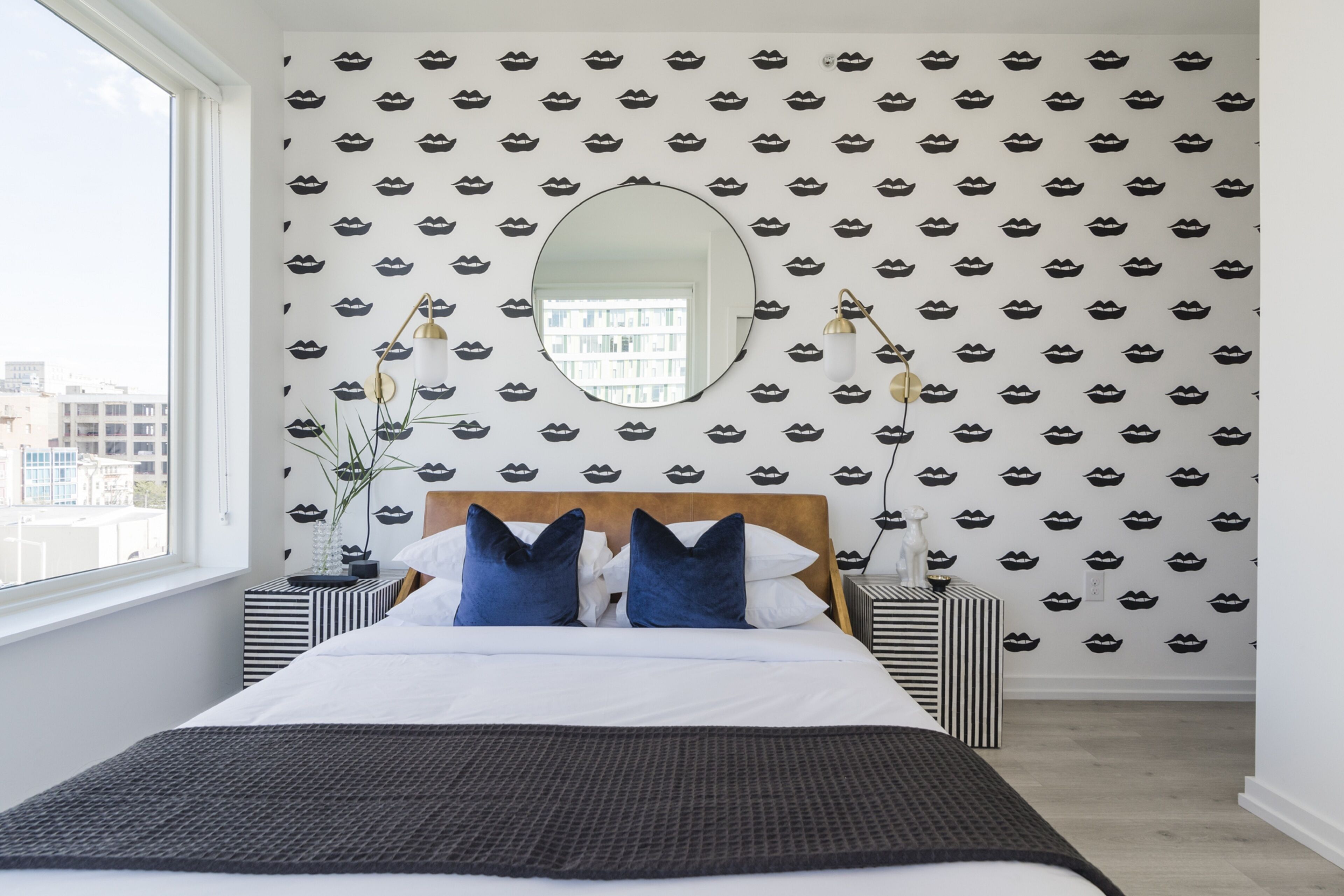 A modern bedroom with a large bed, a round mirror, and patterned wallpaper.
