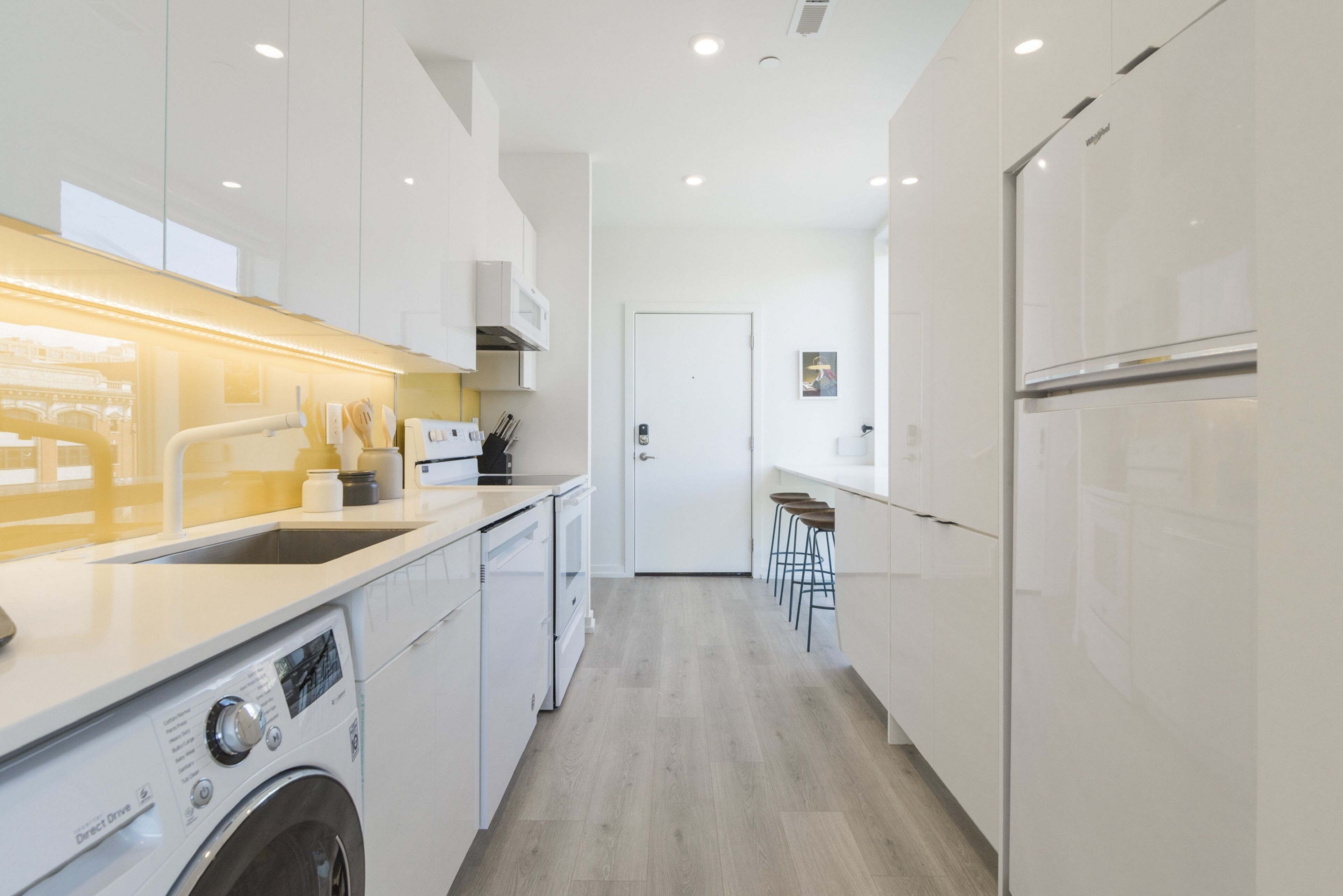 Una cocina moderna con armarios blancos, lavadora integrada y refrigerador de acero inoxidable.