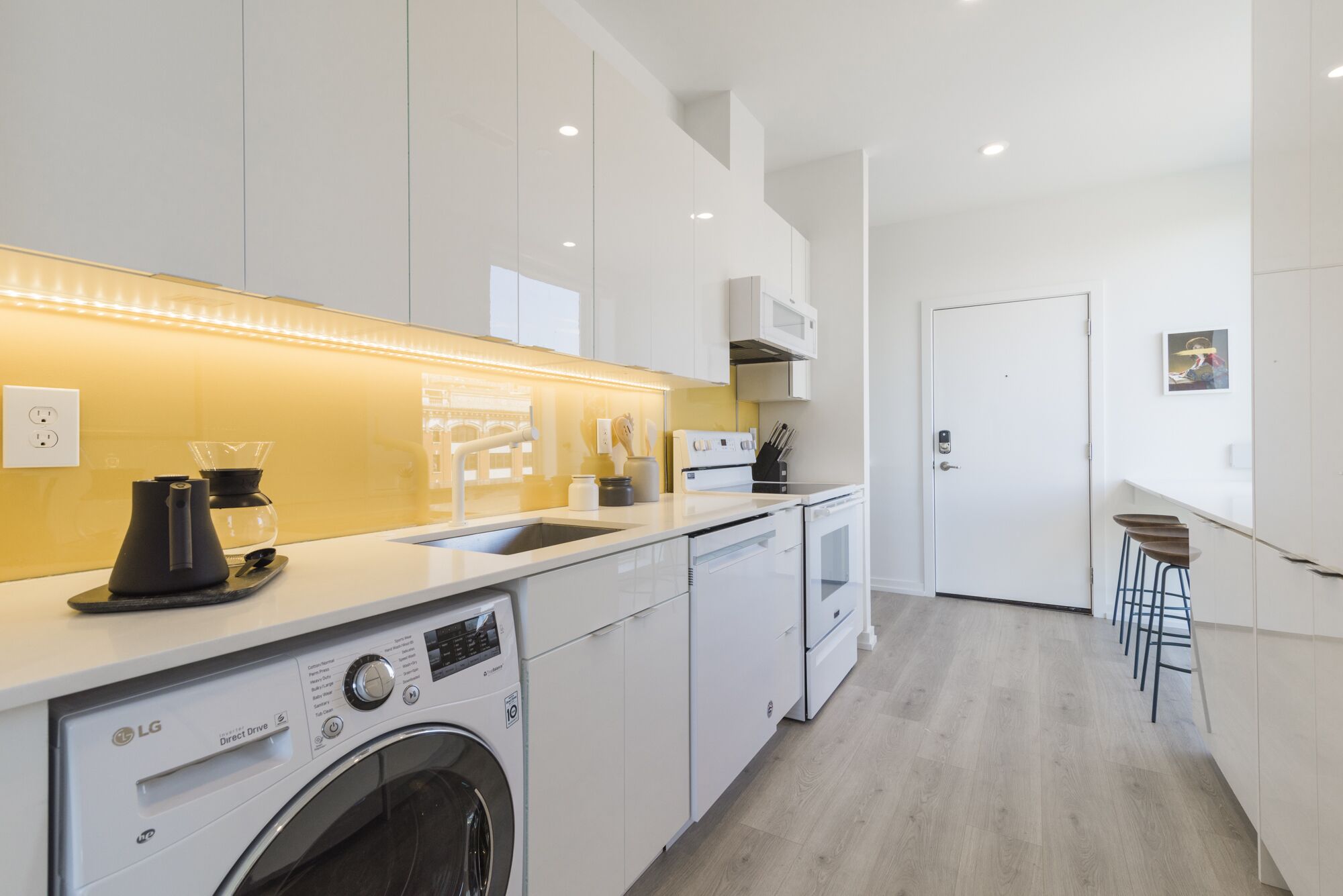 A modern kitchen with a washing machine, a coffee maker, and a microwave.