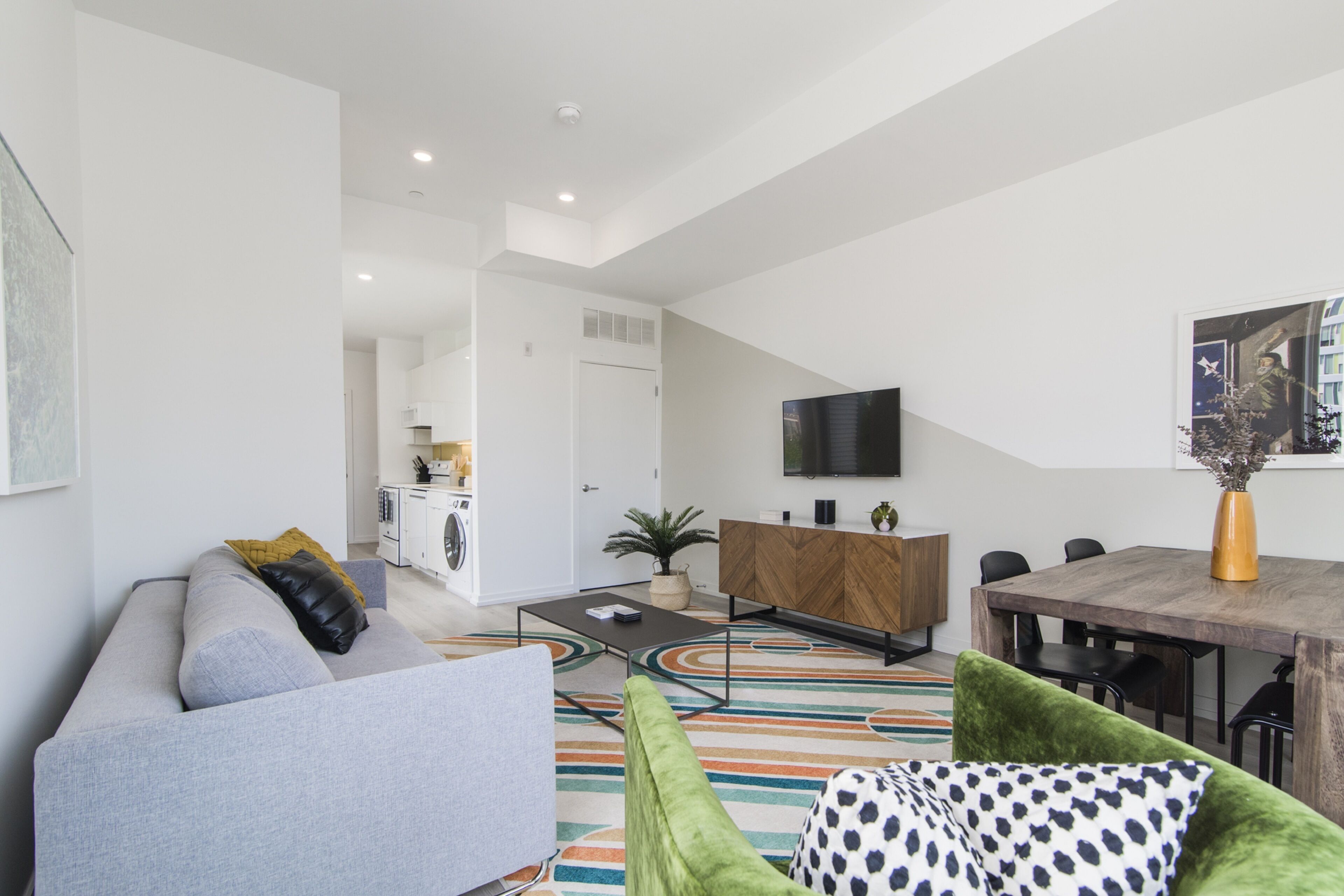 A modern living room with a grey sofa, a green armchair, and a dining area with a wooden table and chairs.