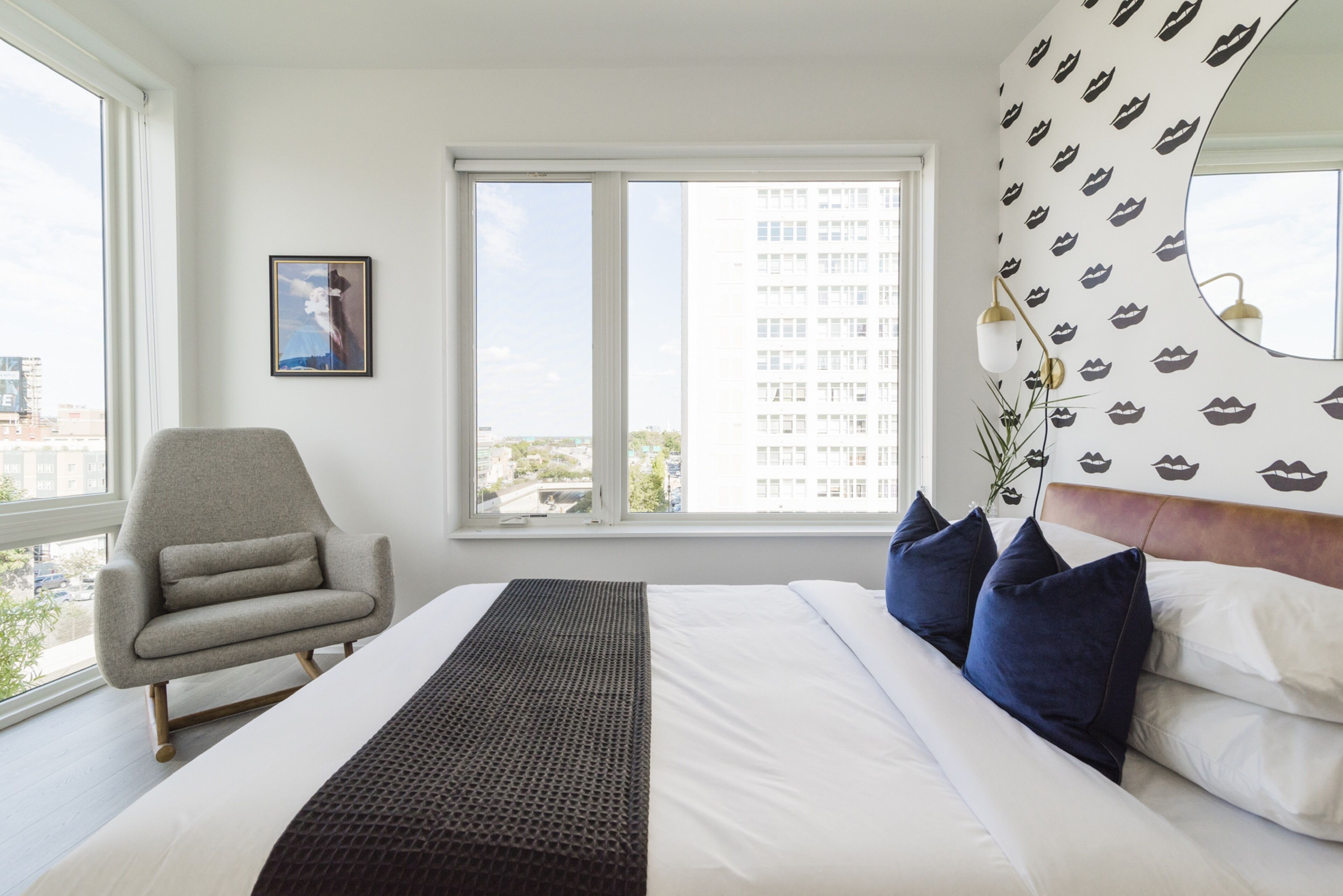 A hotel room with a bed, a chair, a window, and a wall with a pattern.