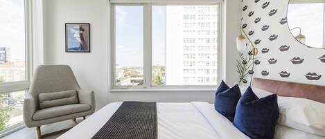 A hotel room with a bed, a chair, a window, and a wall with a pattern.