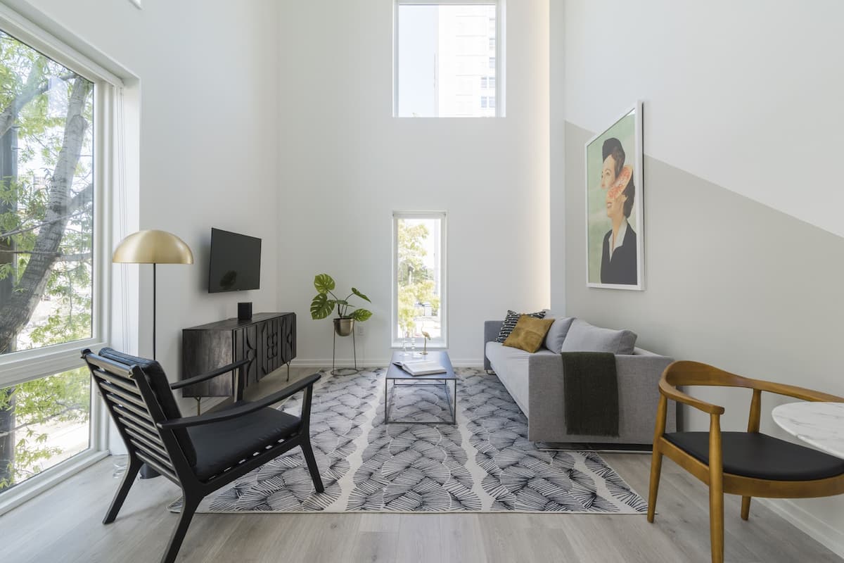 A modern living room with a sofa, chairs, a coffee table, and a TV. There is a window with a view of trees and a painting on the wall.