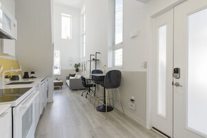 Una cocina moderna con electrodomésticos blancos, una zona de comedor con mesa y sillas, y un pasillo que conduce a una puerta.