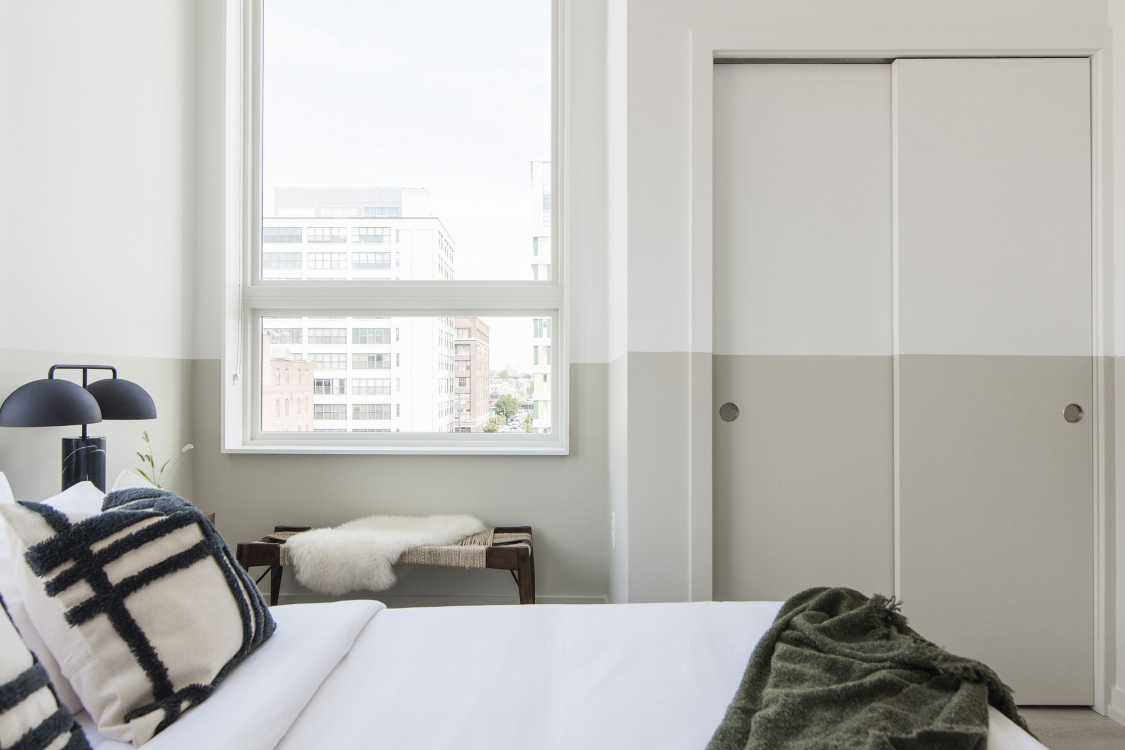 Ein Schlafzimmer mit einem Bett, einem Fenster, einem Nachttisch, einer Lampe und einem Kleiderschrank.