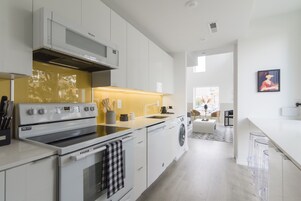 Una cocina moderna con armarios blancos, horno empotrado y lavadora.