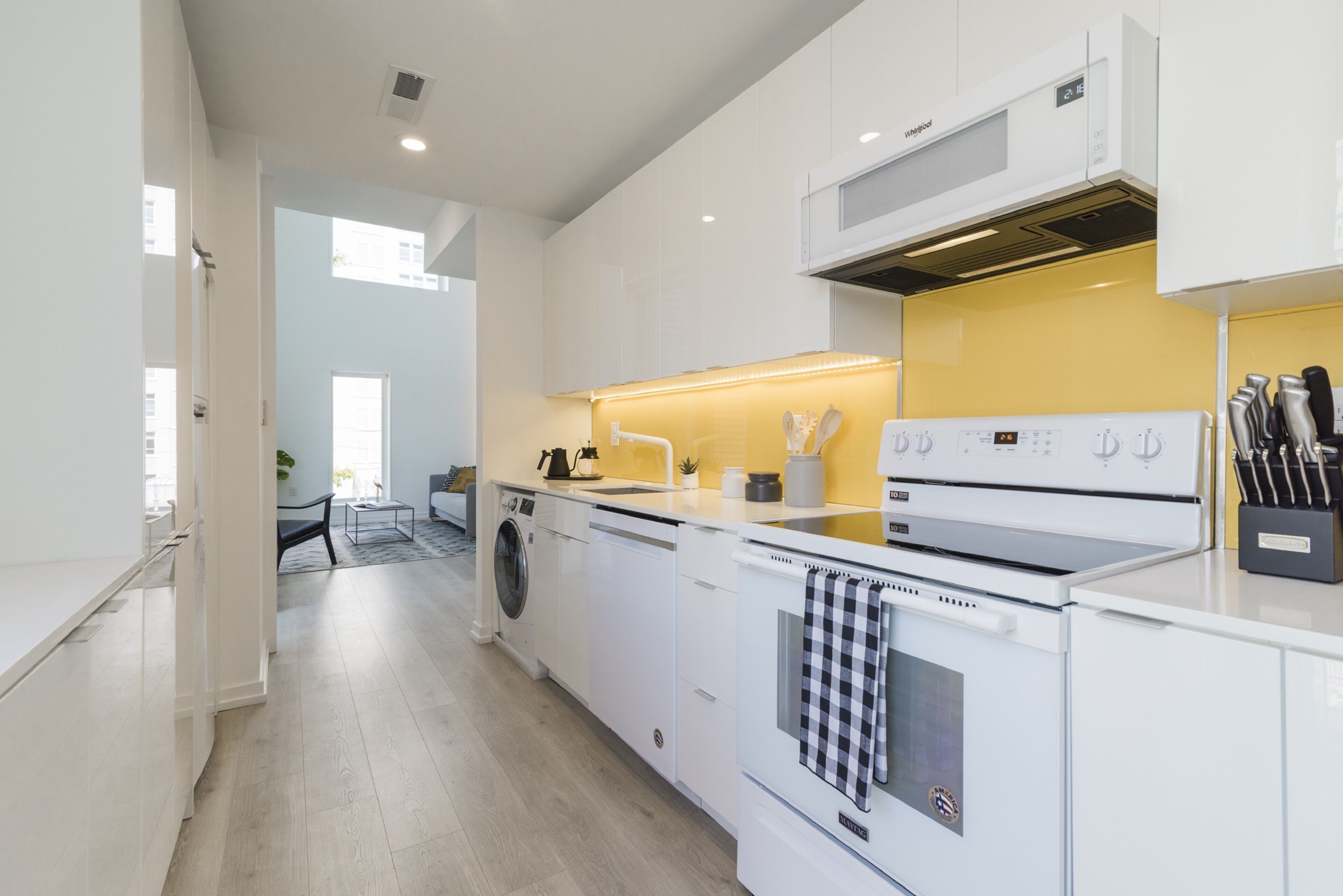 A modern kitchen with white appliances, a washing machine, and a yellow accent wall.
