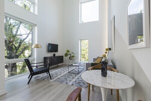 Una sala de estar moderna con un ventanal grande, un televisor de pantalla plana, una mesa de comedor y un sofá.