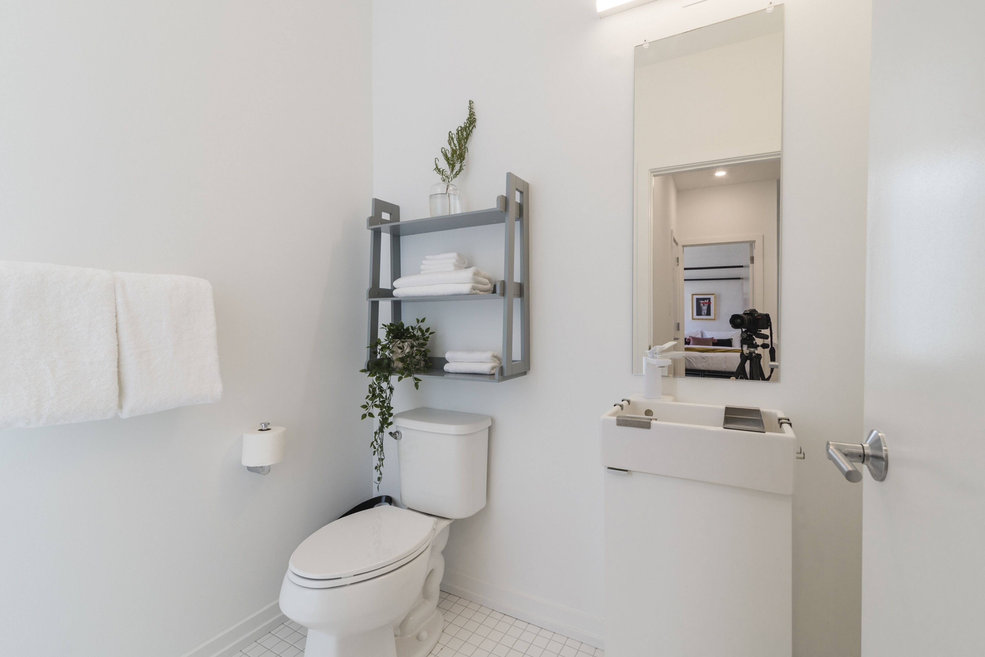 A modern bathroom with a toilet, a shelf with towels, a toilet paper holder, and a mirror.