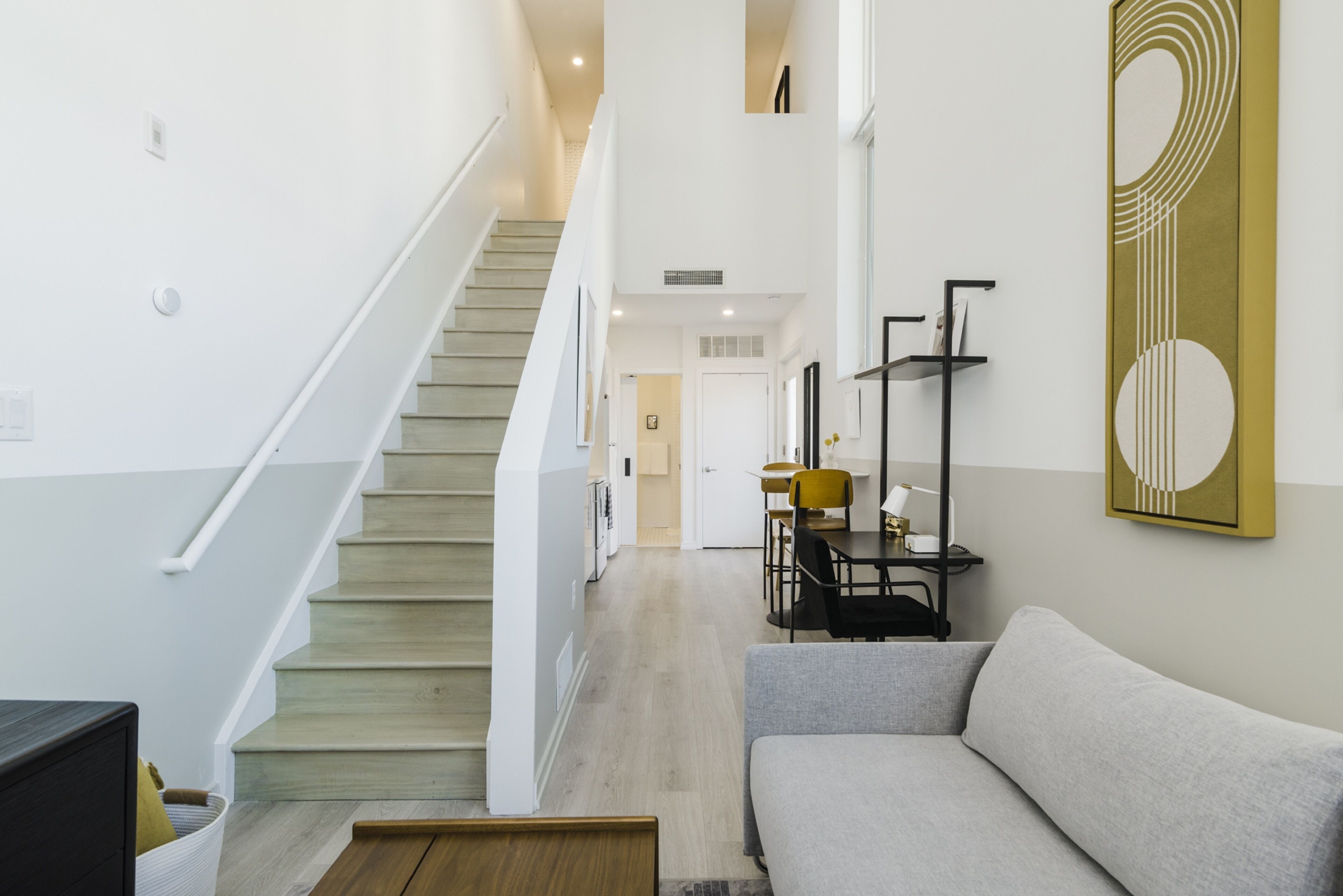 A staircase leading to a second floor, a grey sofa, and a wall with a geometric art piece.