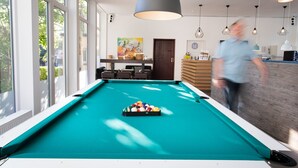 A pool table in a bright room with large windows, a wooden bar area, and modern pendant lighting. - 🏨 SOVA Guesthouse Kassel 🌾 own hotel for up to 18 people (Kassel)