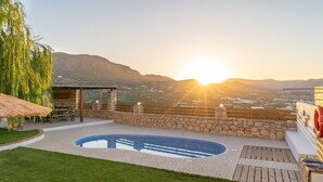 Un espace piscine agrémenté d’un mur en pierre, d’une terrasse en bois et offrant une vue sur la mer au coucher du soleil.