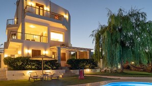 Une maison moderne à deux étages, dotée d’une piscine, d’un espace extérieur aménagé et d’un grand arbre.