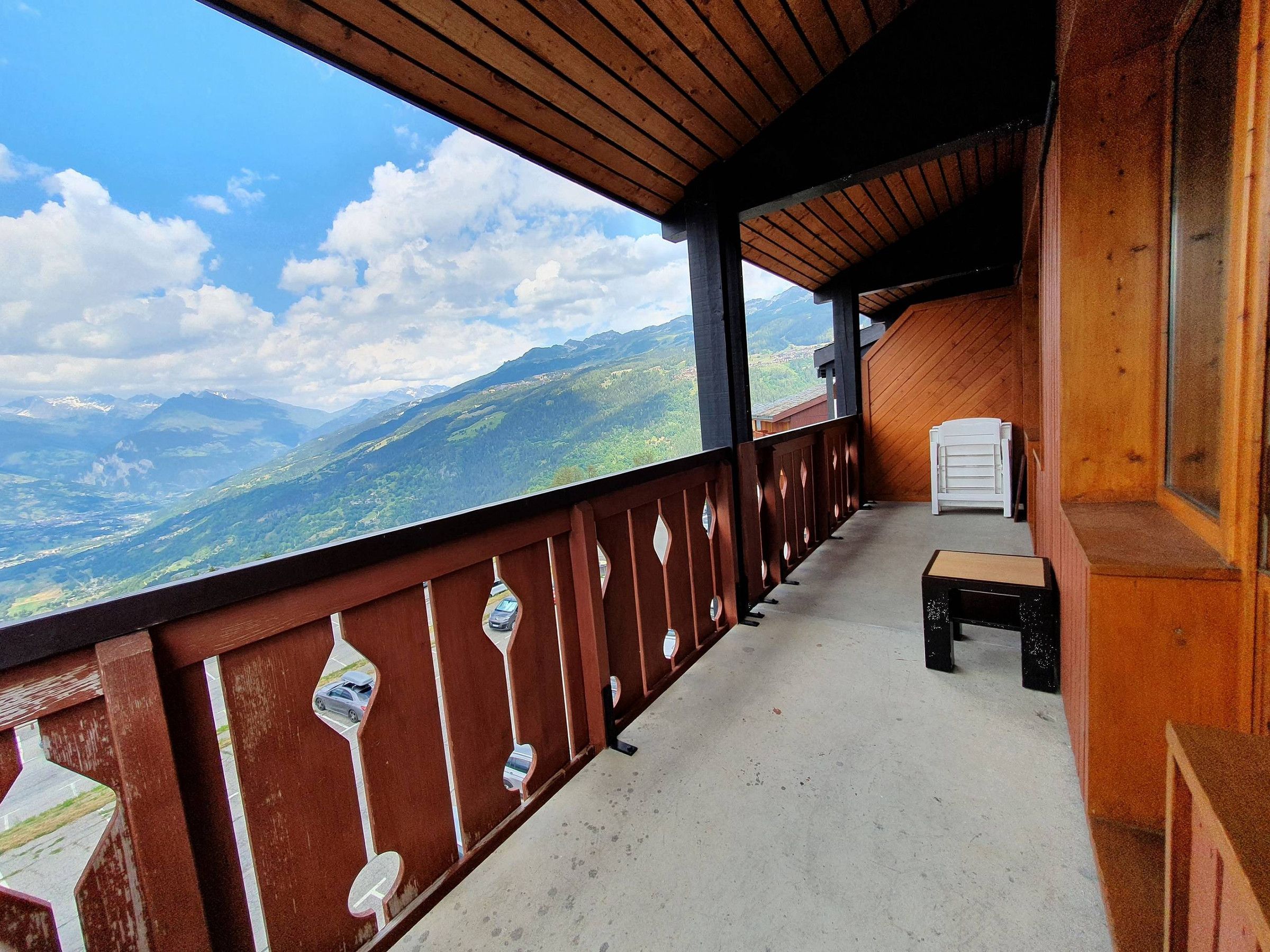 A balcony with a view of mountains, a wooden railing, and a small table.