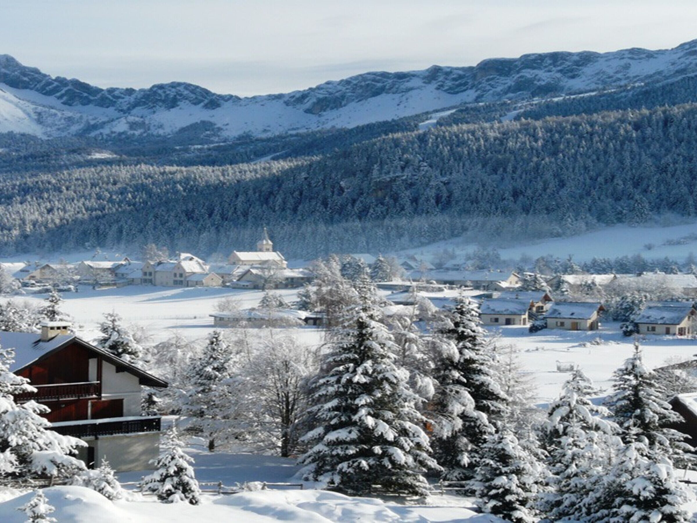 Een besneeuwd dorp met huizen en een kerk, omgeven door bergen.