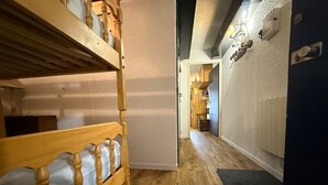 Un couloir étroit au plancher en bois, avec des lits superposés sur le côté gauche et une porte donnant sur une autre pièce.