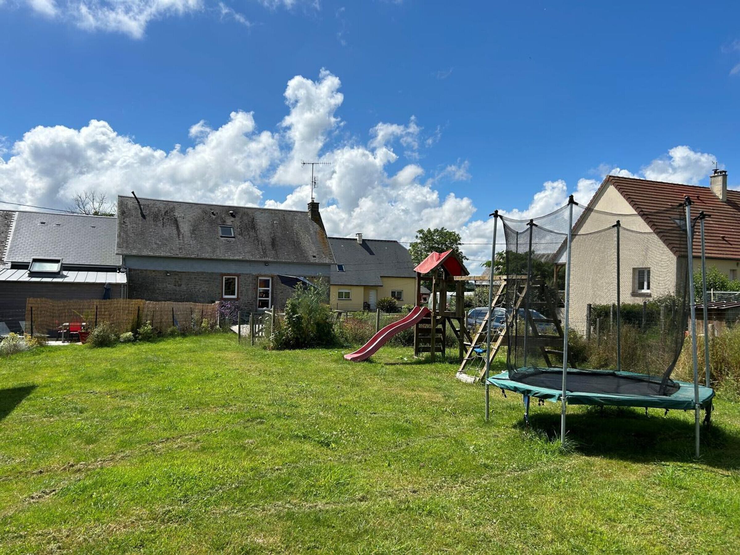 Ein Wohngarten mit Trampolin, Rutsche und Spielhaus.