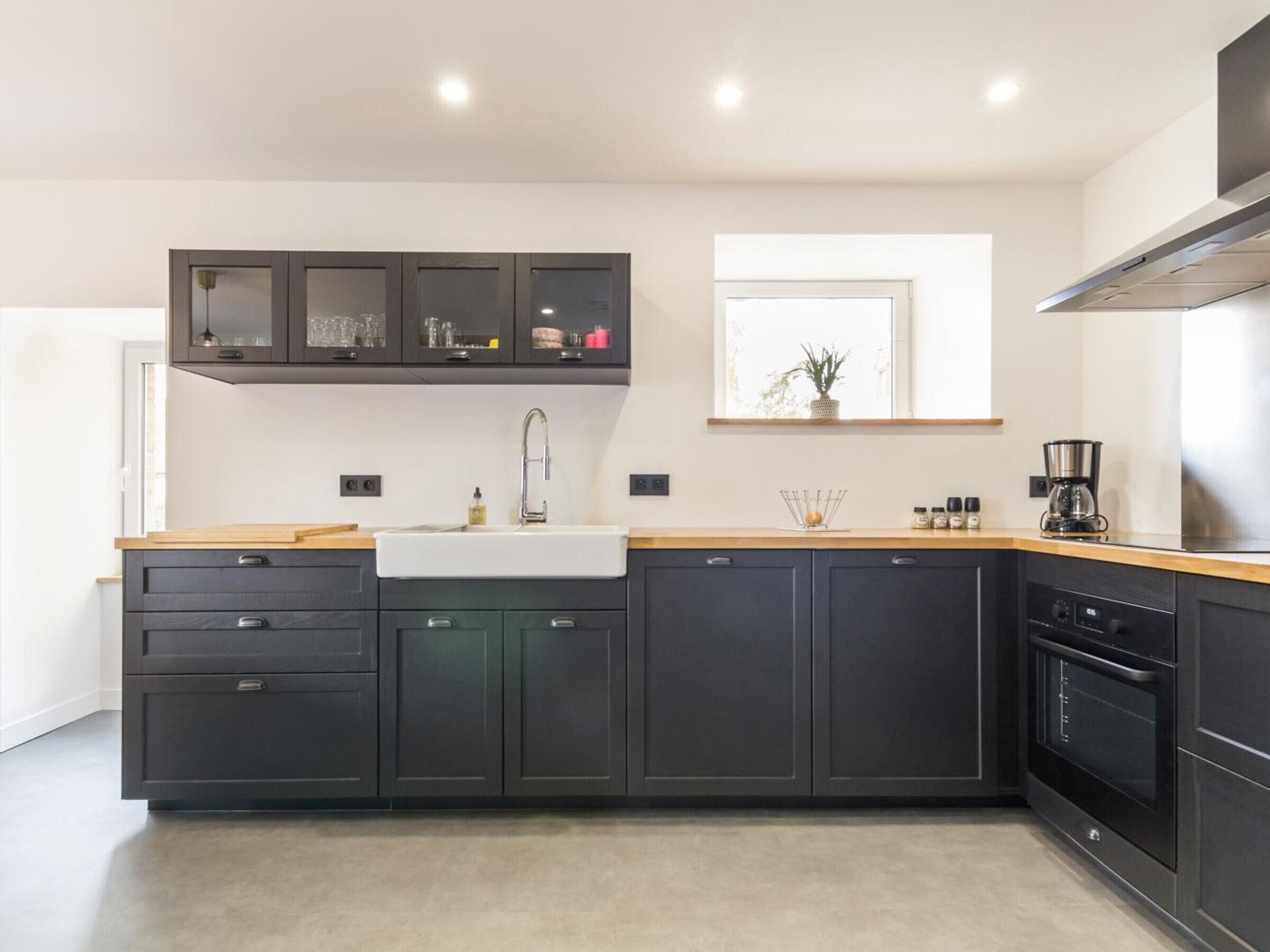 A modern kitchen with dark cabinetry, a wooden countertop, a stainless steel range hood, and a built-in oven.