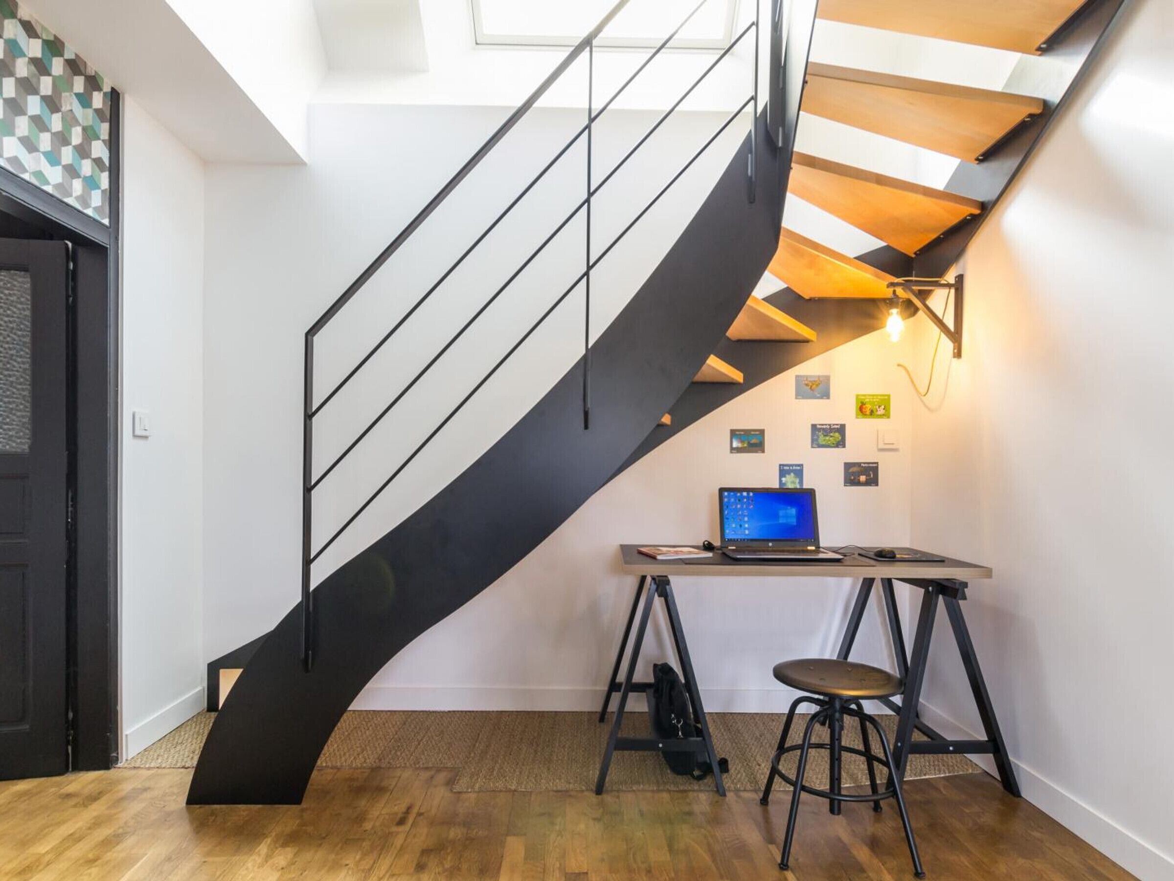 A modern interior with a spiral staircase, a laptop on a desk, and a small stool.