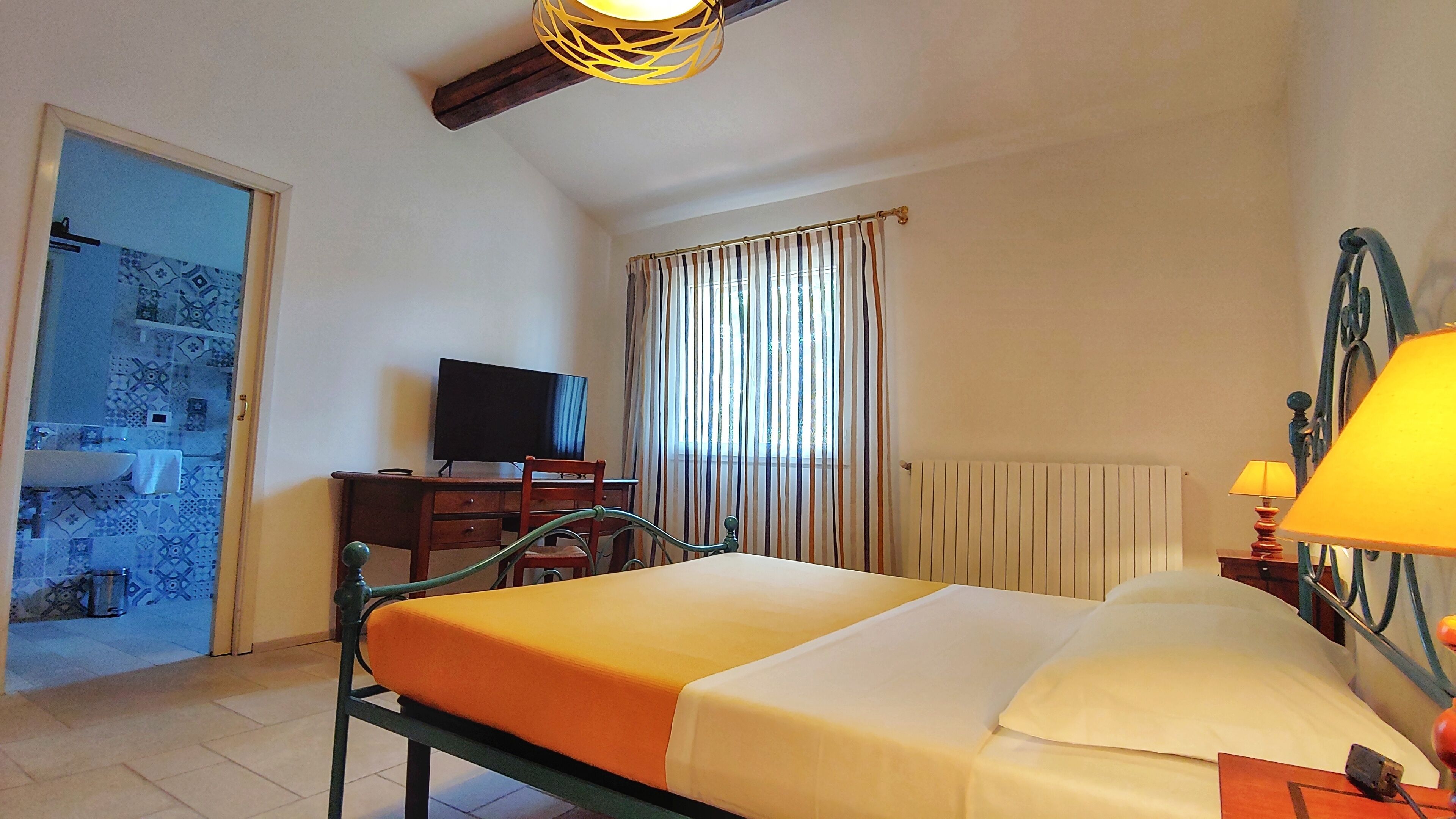 Un dormitorio con una cama, un escritorio con televisor, una ventana con cortinas y una lámpara.
