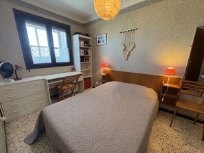 A bedroom with a bed, desk, chair, bookshelf, and a macrame wall hanging.