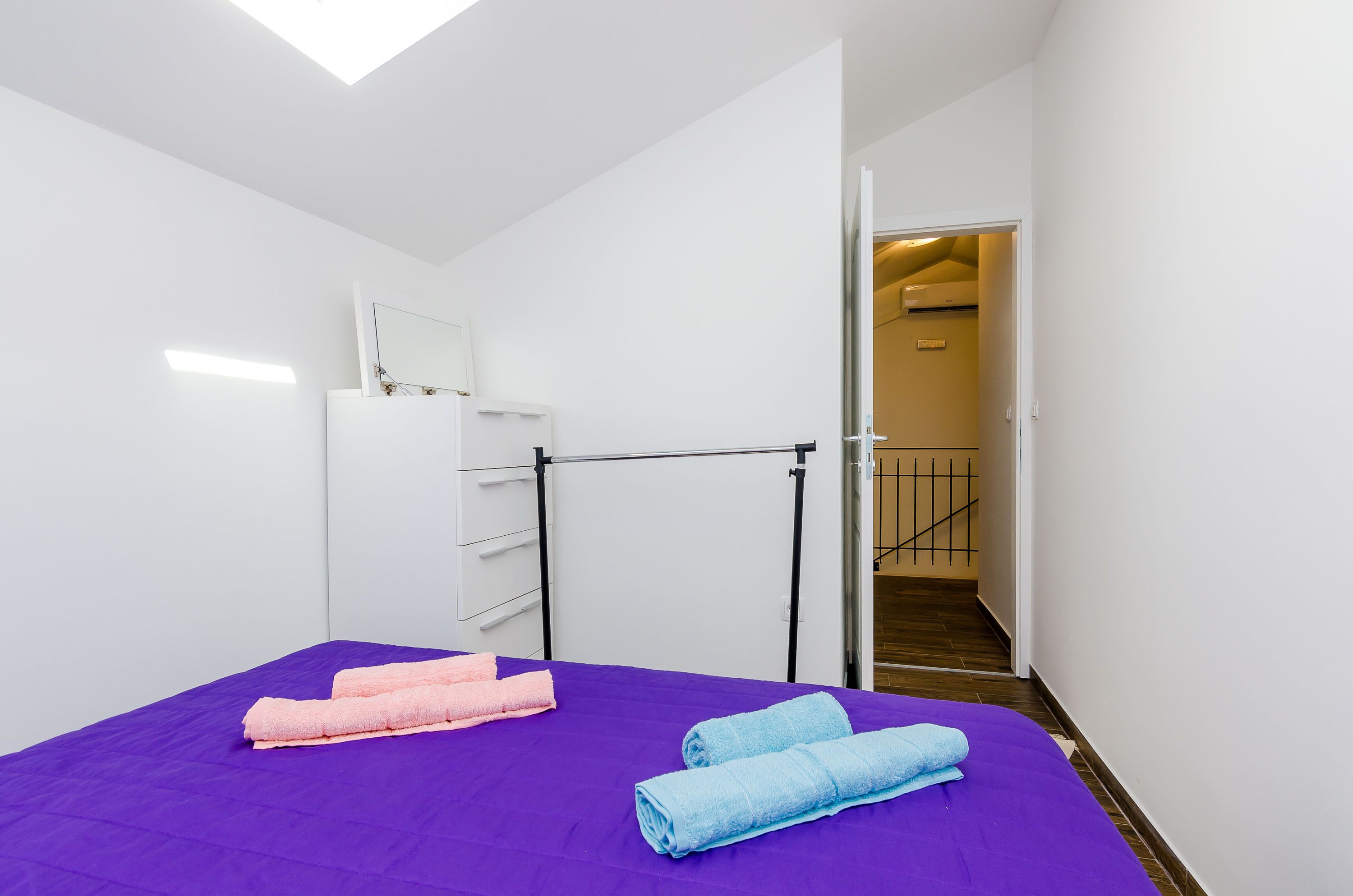 Une chambre d’hôtel avec un lit, deux serviettes, une armoire blanche et une porte donnant sur un escalier.