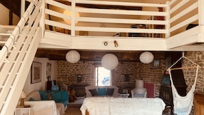 Een gezellige slaapkamer met een entresol, stenen muren, een hangmat en een groot bed.