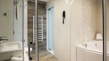 A modern bathroom with a glass shower enclosure, a white bathtub, and a toilet with a towel rack.