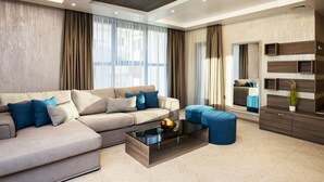 A modern living room with a sectional sofa, a glass coffee table, and a blue ottoman. - Family Hotel Business Club (Shumen)