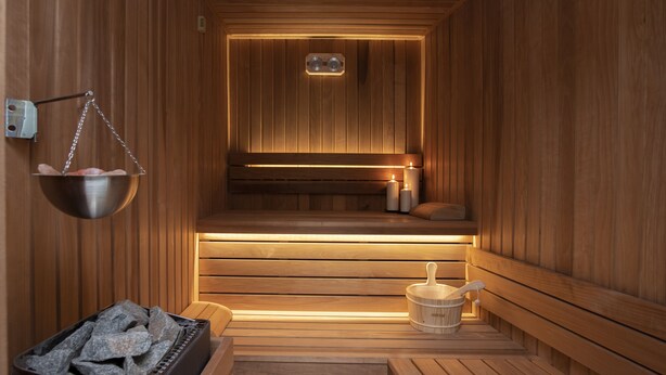 A sauna with wooden walls, benches, a hanging bucket, and a candle. - Family Hotel Business Club (Shumen)