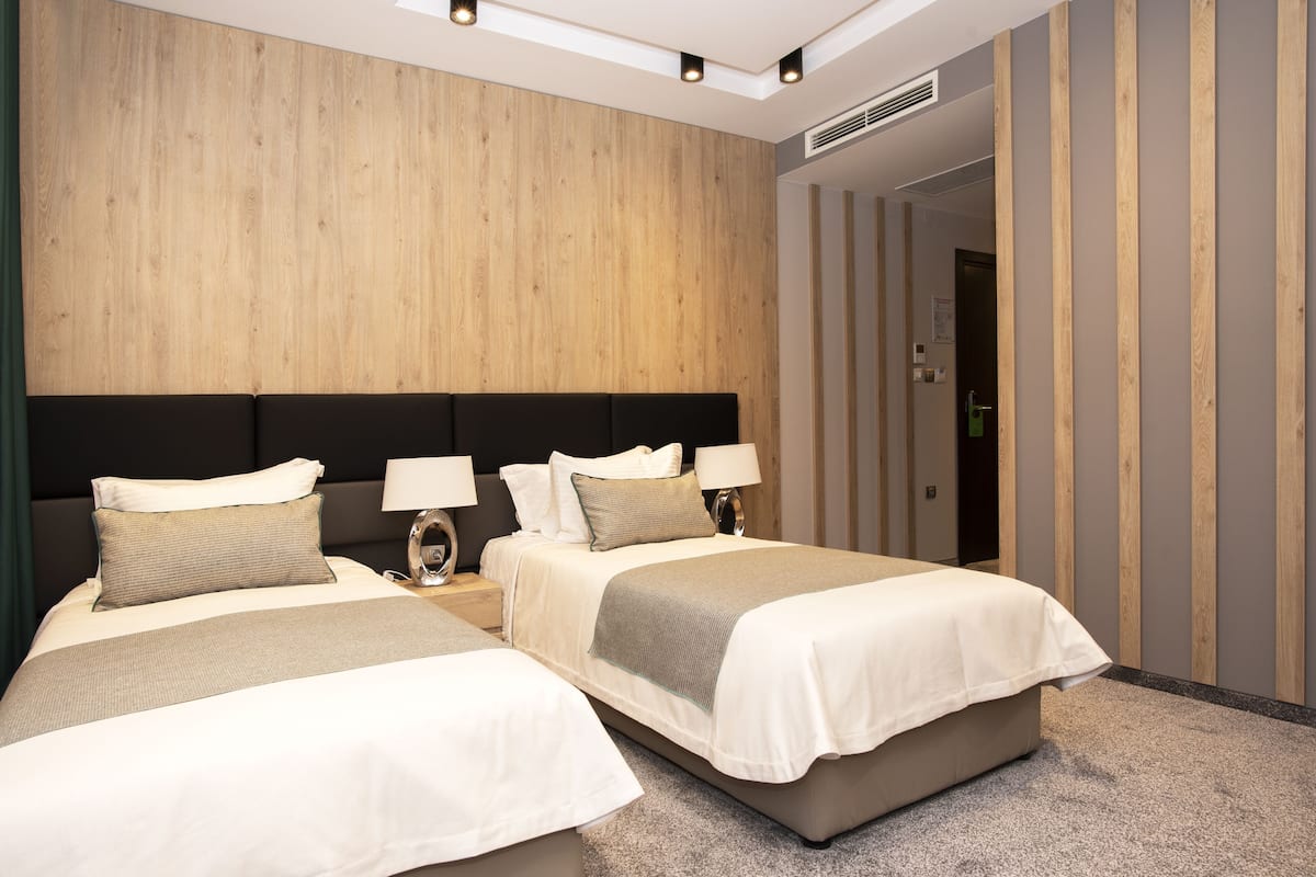 A hotel room with two beds, a wooden headboard, a carpeted floor, and a door leading to another room.
