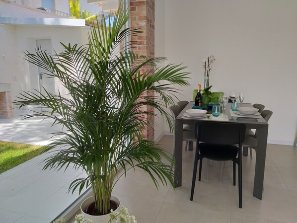 A dining area with a table set for two, a potted plant, and a view of the street outside.