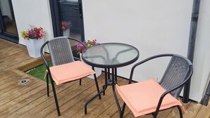 En uteplats med två stolar och ett bord, en vit vägg och en dörr.