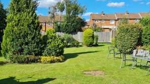 A well-maintained garden with a lawn, various shrubs, and a metal table with chairs. - 1 Bedroom Annex - 2 Mins From Train Station (Harlow)